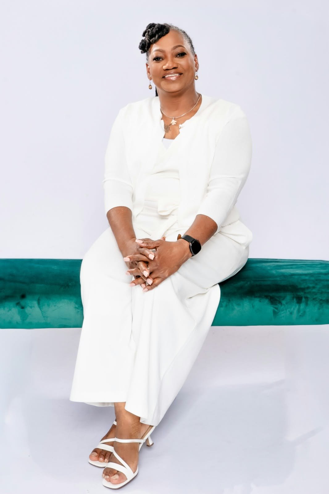 A smiling woman in white sitting on a green upholstered bench.