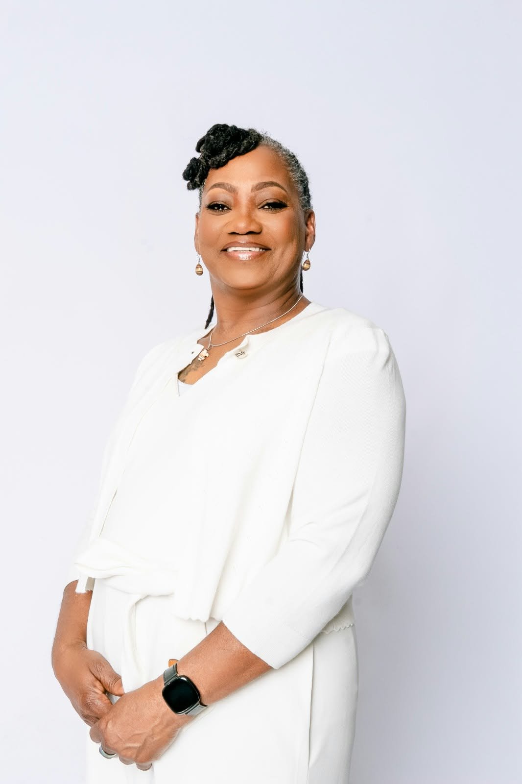 A smiling woman in white, standing with her hands gently clasped.